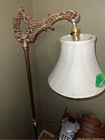 Close-up showing the ornate metal arm and cream fabric lampshade with visible wear and patina.