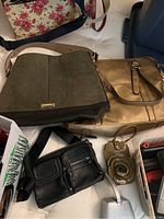 View of various purses laid out including green and black leather purse, metallic gold purse, black leather crossbody, floral canvas bag, and small purses.