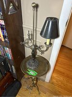 Full view of brass plant stand with tripod claw feet holding a vintage black metal lamp with black shade.