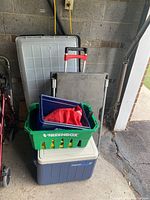 Full view of all items stacked together: two moving dollies behind, green plastic crate on cooler, large underbed bin behind all.