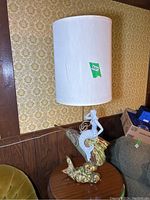 Photo of vintage Royal Haeger ceramic lamp with white lampshade sitting on round wooden table next to sofa