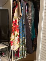 Photo showing a variety of floral and patterned blouses and a quilted brown garment hanging in a closet next to a TV.