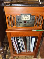 Clear photo of the wooden record player unit showing the integrated radio with large tuning dial, speaker grills on both sides, and a storage area beneath holding vinyl albums.