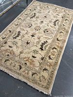 Full view of beige rug with central floral medallion and floral vine border