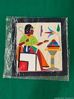 Cushion cover packaged in clear plastic showing embroidered Egyptian figure and bird motif.