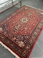 Full view of red field rug with ivory fringe and metal table support visible