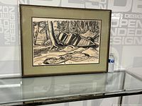 Framed ink drawing with boat on shoreline displayed on glass surface with background text.