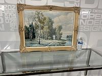Full view of the framed landscape print with birch trees and water body on a glass table with water bottle for scale.