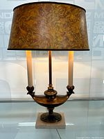 Front view of English style table lamp with marbled shade and two faux candle bulbs on a marble base.