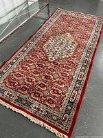 Full view of red Persian rug laid on concrete floor near glass table