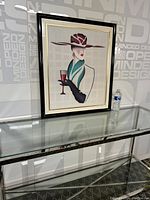 Framed watercolor painting displayed on glass table with water bottle for size reference.