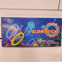 Photo of the box containing 100 pieces of 20cm neon glow sticks and 100 connectors, colorful marine-themed packaging.