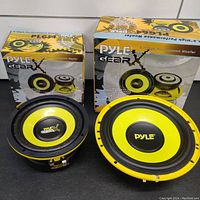 Two Pyle Gear high performance woofers with black and yellow cones, shown with their original packaging boxes on a black surface against white background.