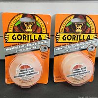 Two unopened packs of Gorilla double-sided mounting tape with bright orange backing card and Gorilla logo featuring a gorilla image.