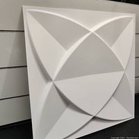 Single white 3D PVC wall panel tile with symmetrical overlapping curved geometric shapes creating a raised petal-like design, matte finish, 12x12 inches, shown standing vertically against wood panels background.