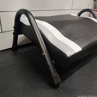 Close-up side view showing the black tubular metal legs and foam footrest surface with white stripes.