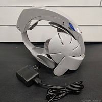 Side view of white electronic neck and head massager with black power supply visible beside it.