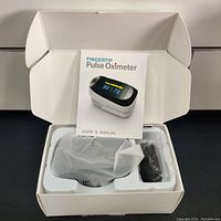 Pulse oximeter device in packaging with user manual on top.