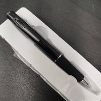 Black spy camera pen in white plastic tray, showing full pen with shiny metal tip and clip area.