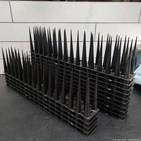 Side and angled view showing stacked black spikes mounted on plastic grid bases, highlighting the length and pointed design of each spike.