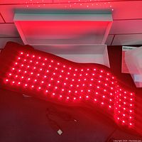 Red light therapy belt powered on emitting red LED light in rows.