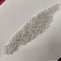 Pile of many small, round silver jump rings spread on white background