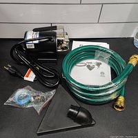 Complete kit laid out: pump, garden hose, funnel adapter, Teflon tape, fittings on black surface.