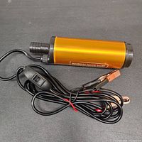 Photo of the portable pump showing orange cylindrical body and attached power cord with battery clamps