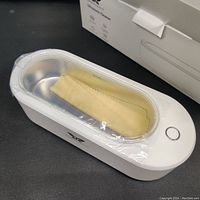 Ultrasonic cleaner with protective plastic on transparent lid and yellow cloth inside cleaning tank.