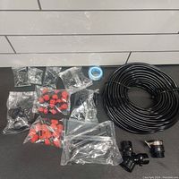 Photo of all irrigation system components including hose, various connectors, nozzles, and adapters, mostly sealed in plastic bags.