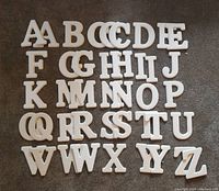 Photo of 43 white beveled alphabet letters arranged on floor, missing letter L, multiple instances of some letters visible, approx. 6 inches tall each.