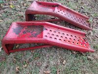 Side view of two red metal car ramps showing rust and peeling paint on grass