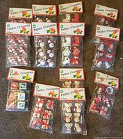 Thirteen plastic bags of holiday mini craft ornaments, each with six ornaments, laid out on floor with vintage-style header cards marked Holiday Ornaments 6 Pack