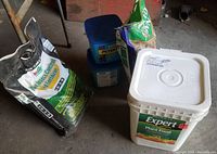 Photo showing bags and buckets of fertilizers and insect control: KGro Lawn Insect Control 28-3-8 bag, two blue Peters Professional Azalea Food buckets, and Schultz Expert Plant Food bucket.