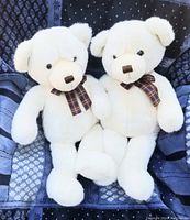 Two white plush Gund bears sitting on a patterned blue quilt, each with a plaid bow tie.