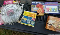 Photo showing a metal turntable organizer, black plastic utensils, Handy Brite work light in box, plastic key organizer kit, painted wooden rooster, and microwave/storage bowl set in box.