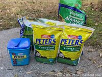 Photo of 3 bags Peters Lawn Food with feeder refill bags, Bayer lawn fertilizer bag, partial crabgrass preventer and fertilizer bag, and Peters Professional Azalea Food tub.