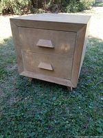 Front view of mid century nightstand showing cube shape, two drawers with wooden angular handles, and blonde finish.