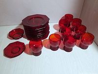 Set of nine octagonal red plates stacked, nine red glasses, and two small dishes arranged on a white surface.