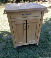 Front view of rolling butcher block cart showing the maple finish, drawer, cabinet doors, and the towel bar on one side.