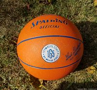 Close-up photo of orange Spalding basketball on grass, showing 'Official' logo, Permalite cover label with '165 N weave quality', and Gale Goodrich signature.