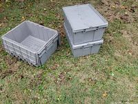 Four gray plastic stacking crates in outdoor grass, two nested/open on left and two stacked/closed on right.