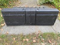 Full view of the black plastic truck bed tool box on a concrete path with grass and leaves around. Shows overall shape and condition.