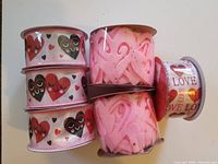 Six spools of Valentine-themed ribbons including three with cartoon heart designs, two pink felt heart-cutout ribbons, and one metallic love-themed ribbon.
