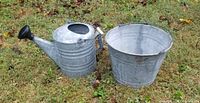 Galvanized watering can and bucket placed on grass showing overall condition and size.