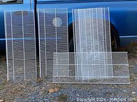 Six vinyl coated steel wire pantry shelves displayed outdoors leaning against a vehicle, shown from front view.