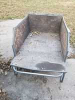 Front view showing aluminum frame with stained plywood base and panels, wooden surface worn and stained, open front area, ground surface visible.