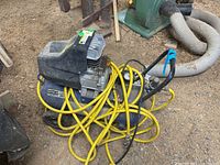 Full view of blue oil-less air compressor with black protective cover, coiled yellow 3/8 inch hose, and metal handle.