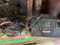 Top view of Craftsman variable speed belt sander and Craftsman carrying bag on wooden surface.