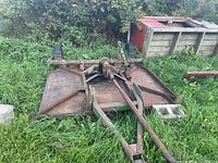 Full view of rotary cutter deck lying in grass beside wooden bins.